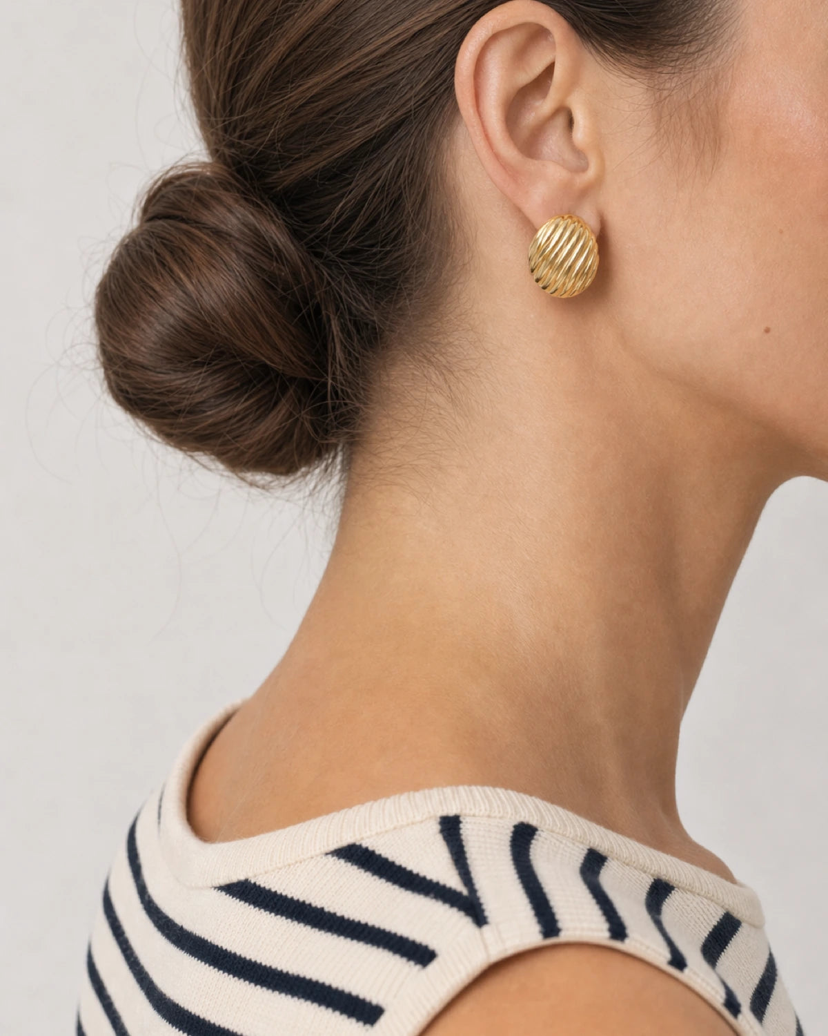 Eye-free rear portrait of Claudia wearing the convex gold Odette oval stud