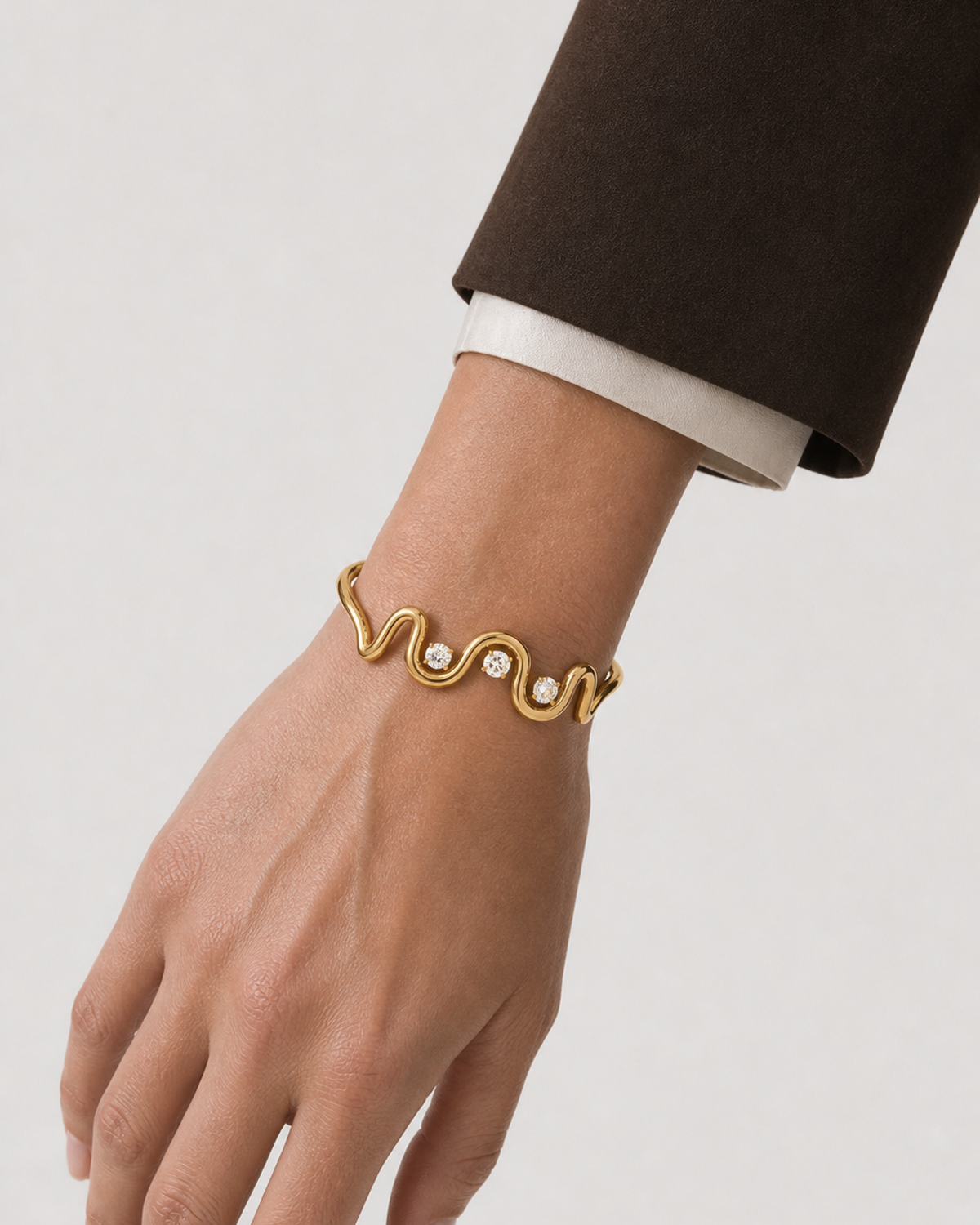 Clean wrist close-up of the Onda gold wave cuff and three clear stones