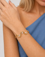 Clean close wearing view of the Onda gold wave cuff and exactly three clear stones