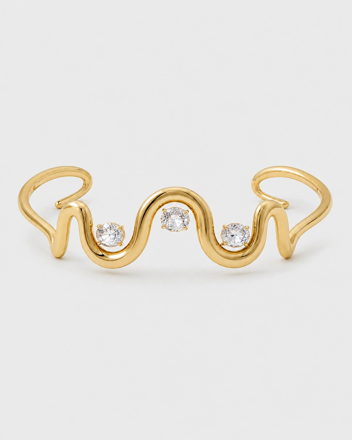 Onda gold crystal wave cuff with three clear stones on a pale neutral-grey studio background