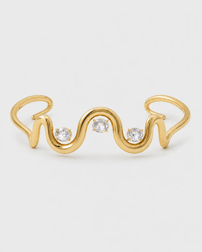 Onda gold crystal wave cuff with three clear stones on a pale neutral-grey studio background