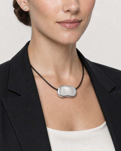 Close neckline view of the Orra mirror-polished silver bean pendant on black cord