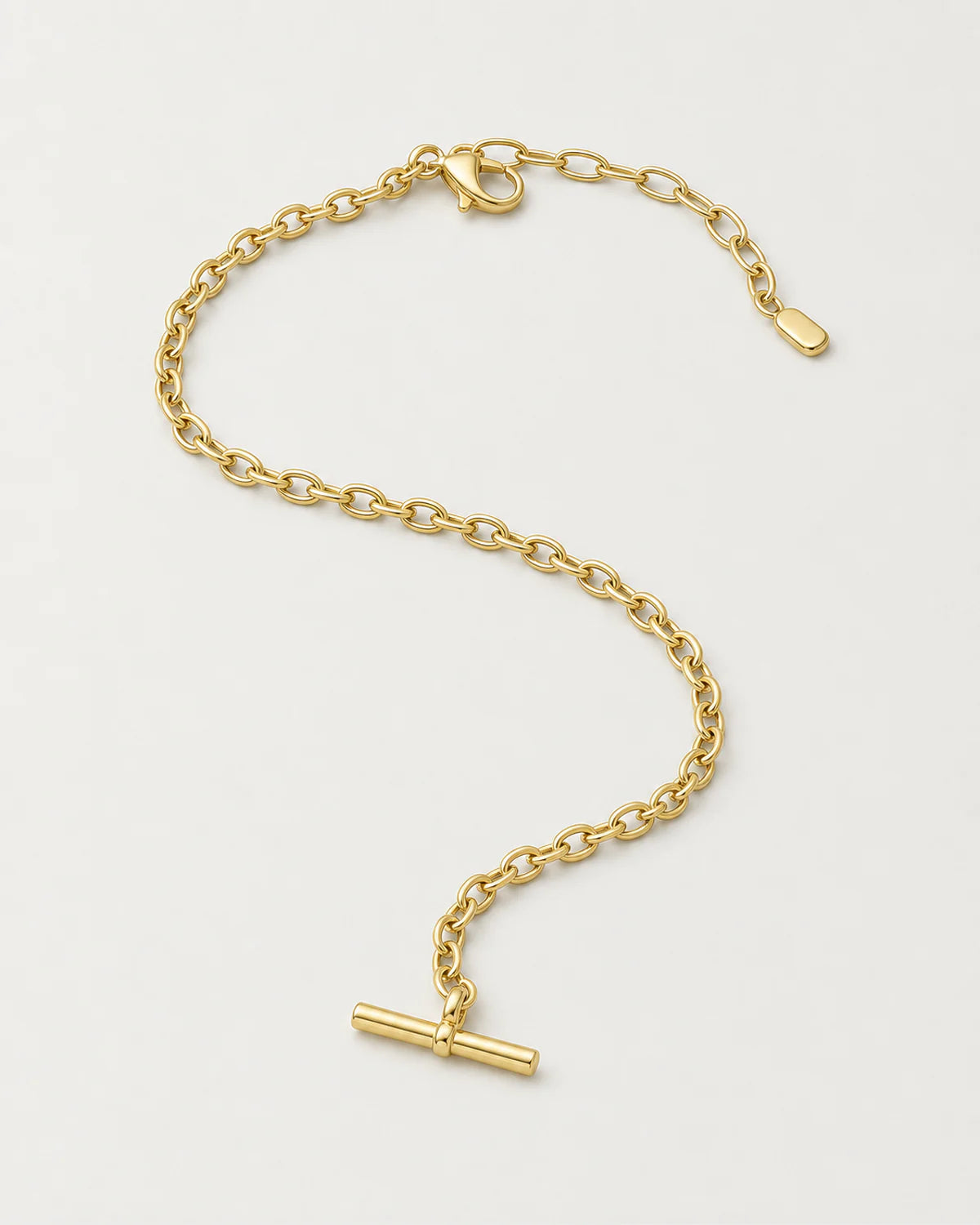 Romy gold-tone T-bar necklace in an alternate curved arrangement on pale grey