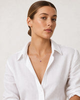 Brunette model in a white Côte d’Azur linen shirt wearing the Rosalie red heart necklace