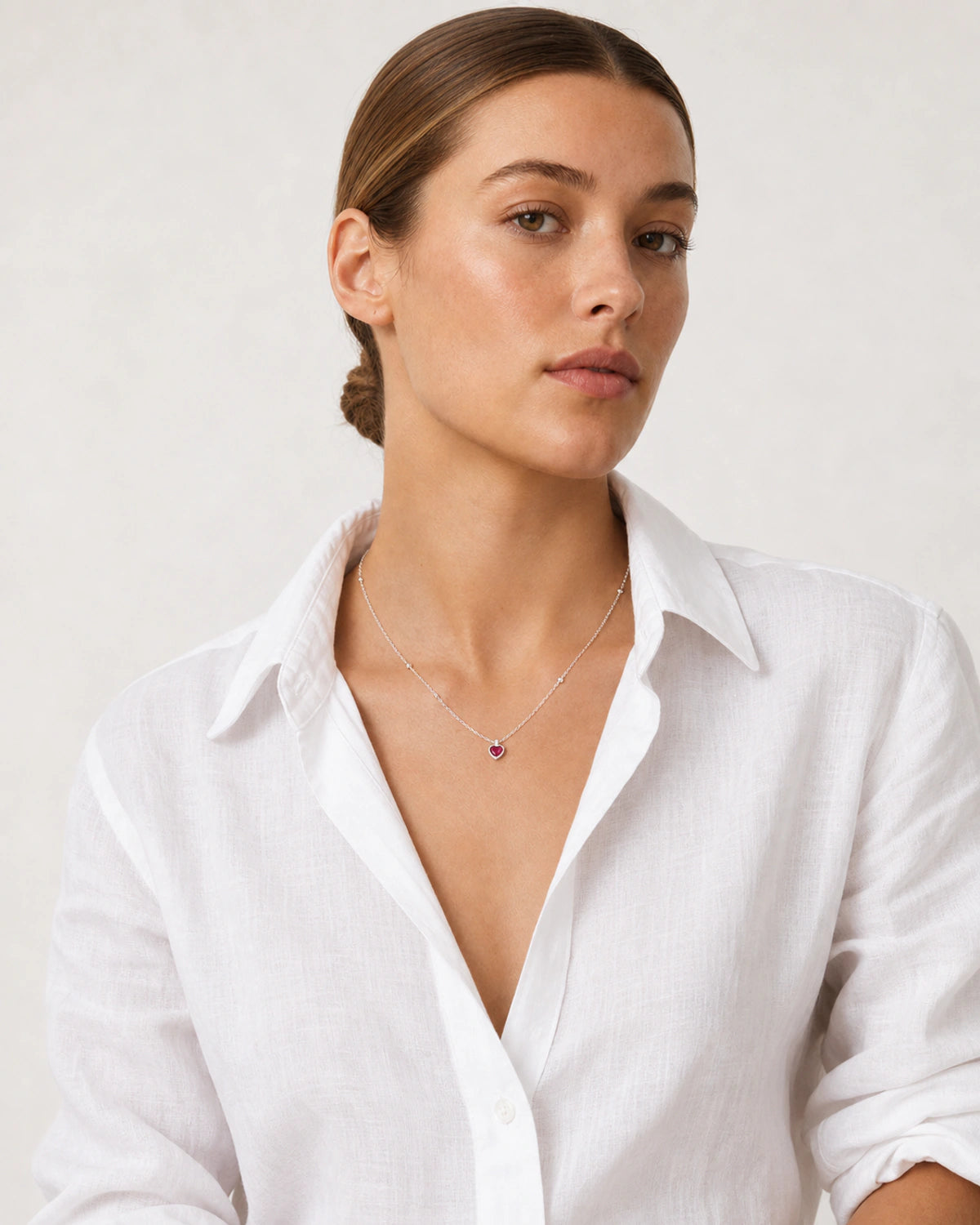 Brunette model in a white Côte d’Azur linen shirt wearing the Rosalie red heart necklace