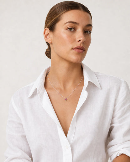 Brunette model in a white Côte d’Azur linen shirt wearing the Rosalie red heart necklace