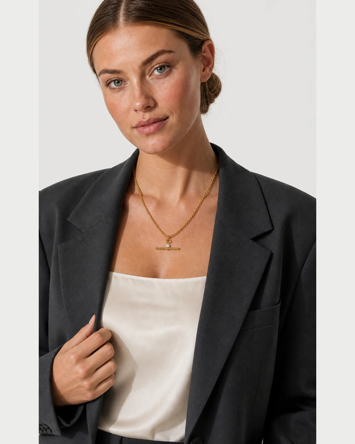 Model holding her blazer lapel while wearing the Sloane gold toggle necklace