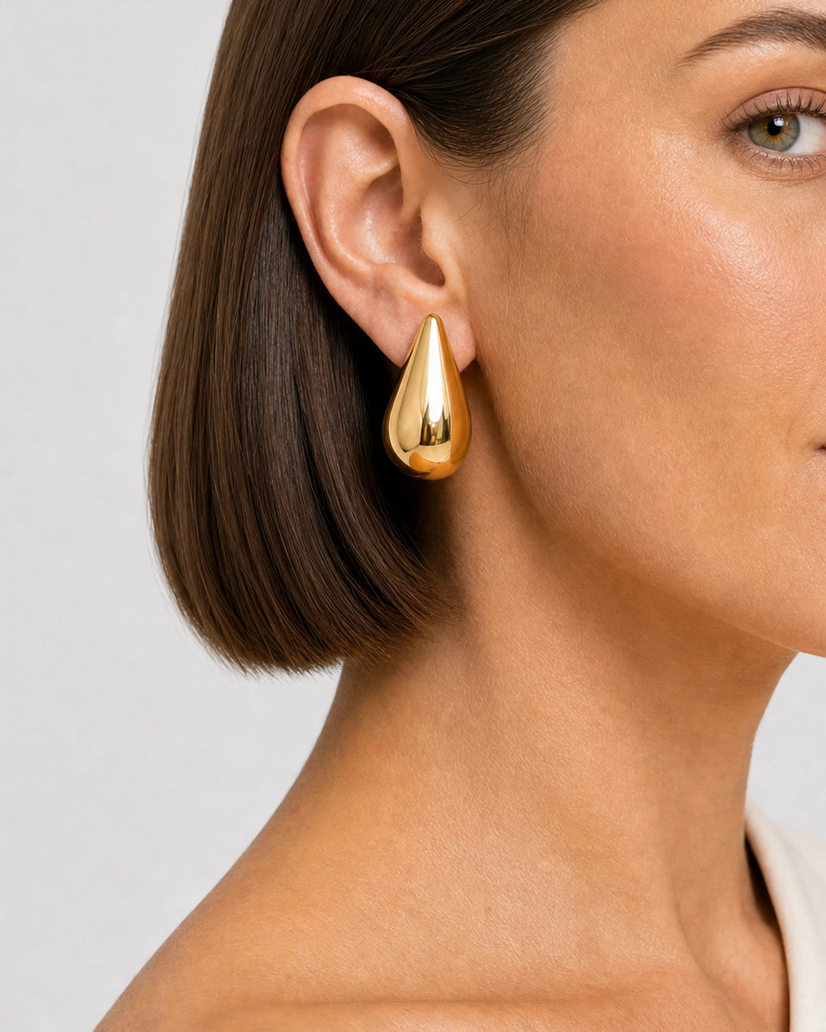 Extreme on-ear macro of the mirror-polished Solène gold teardrop stud
