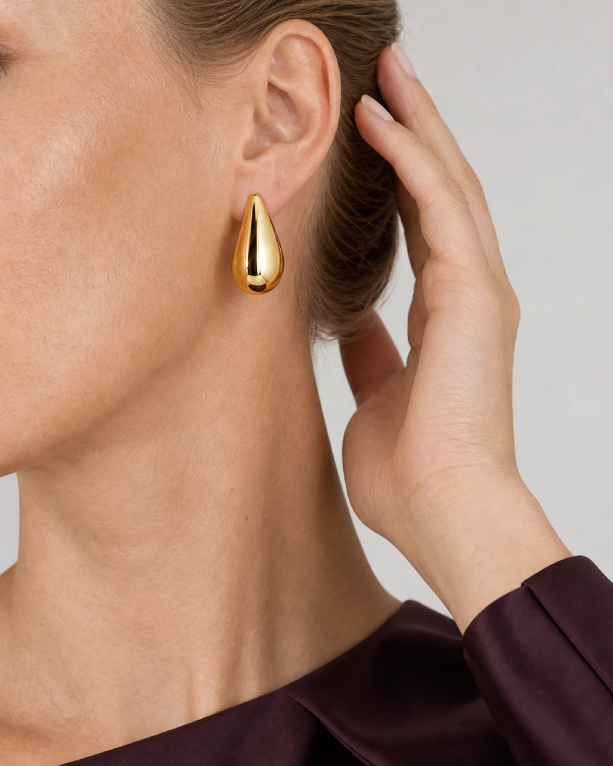Eye-free hair gesture beside Lydia's gold Solène teardrop earring
