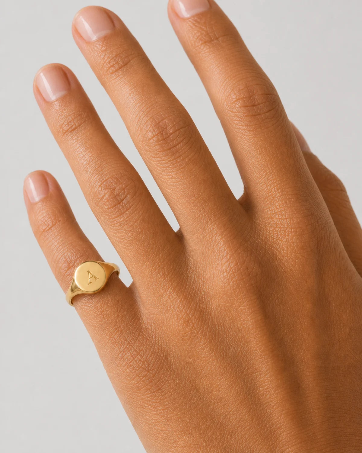 Clean on-hand close-up of the Solenne oval signet engraved with A