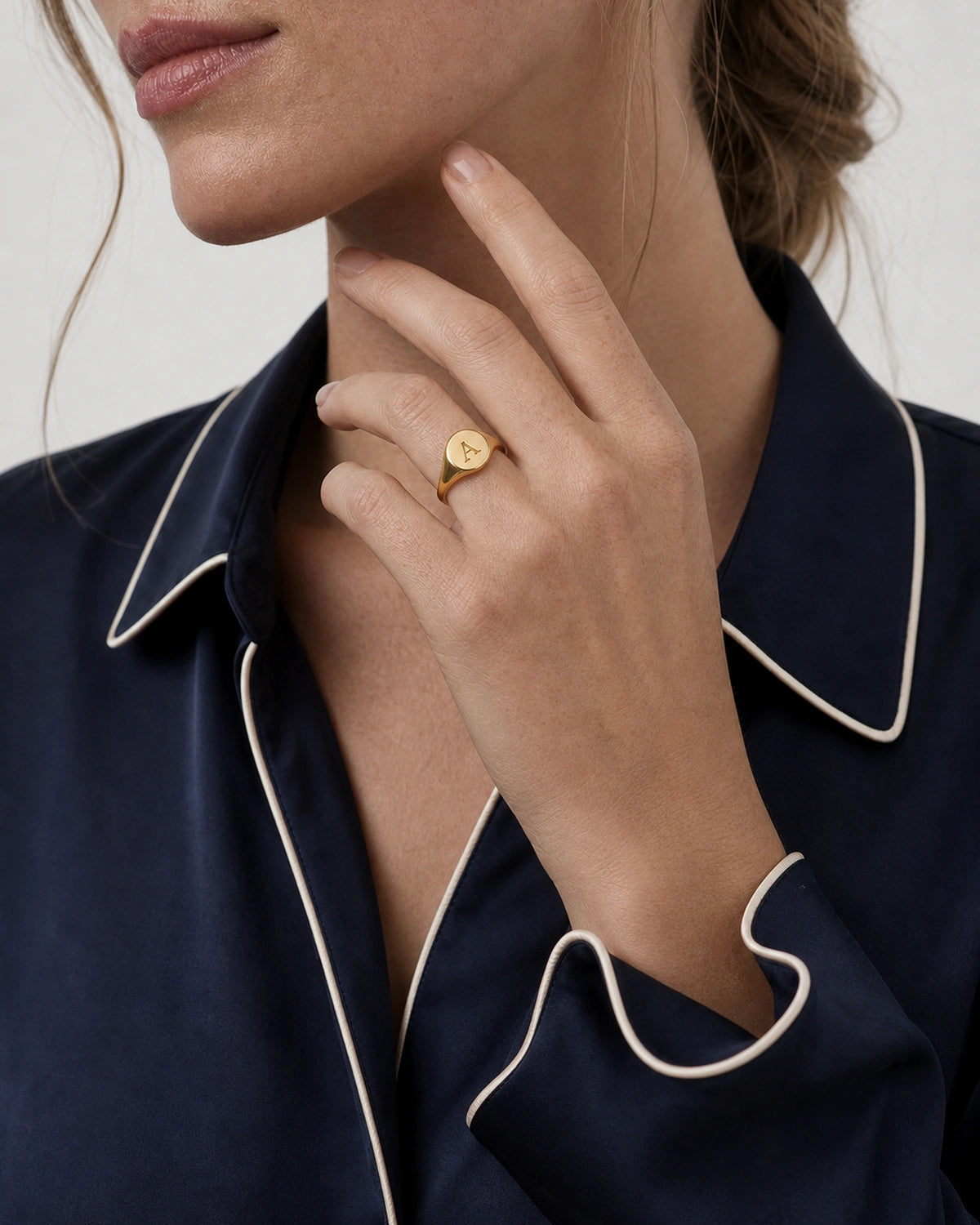 Chin-down hand pose wearing the gold Solenne initial A signet ring