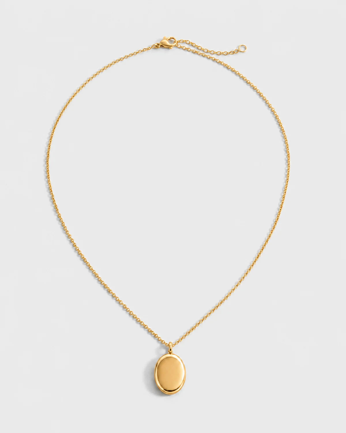 Solenne blank gold oval pendant necklace on a seamless pale dove-grey studio background