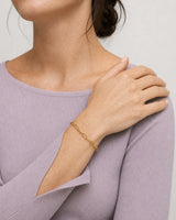 Crossed-wrist wearing view of Vela gold paperclip bracelet