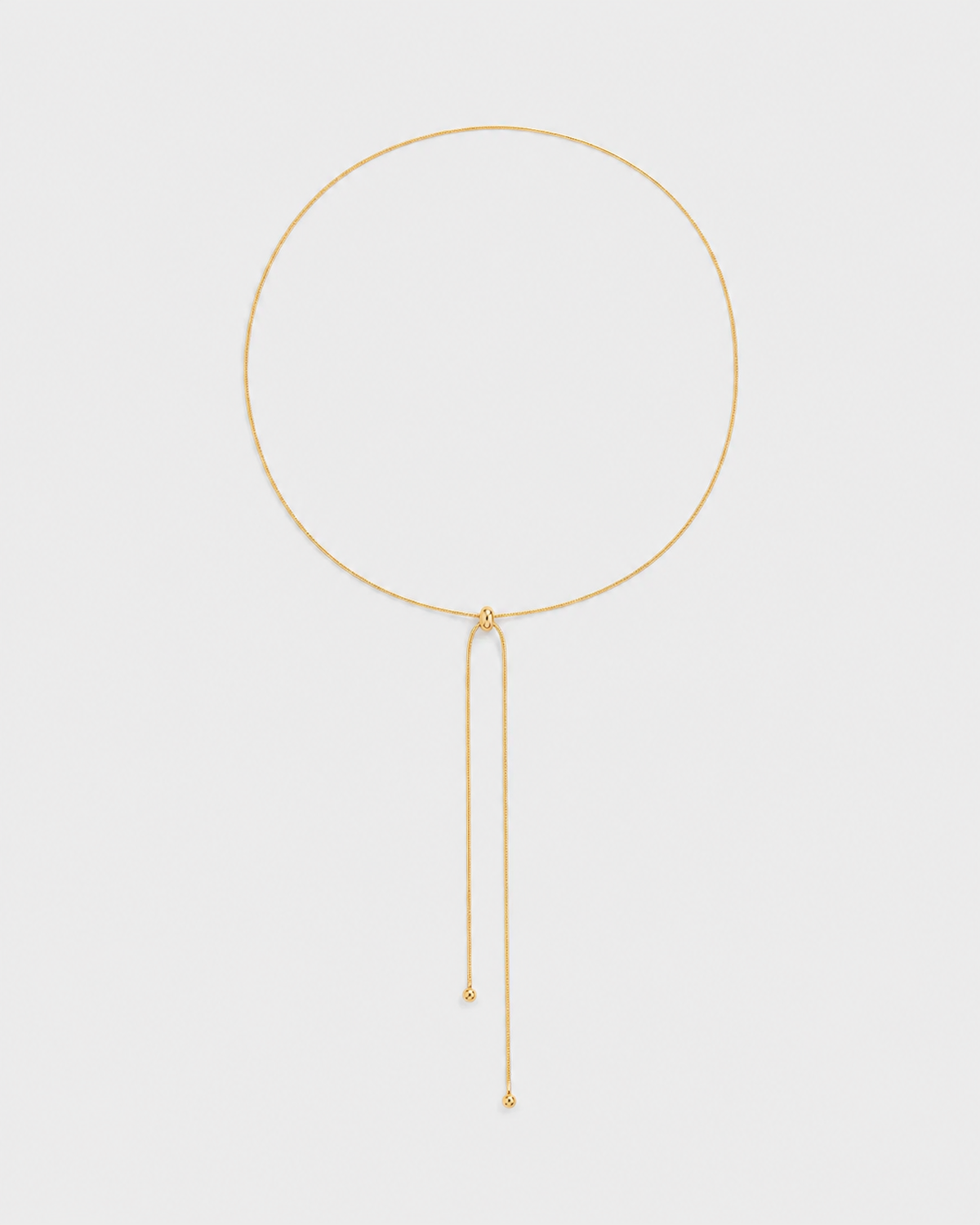 Vela fine gold slider lariat necklace on a seamless pale dove-grey studio background