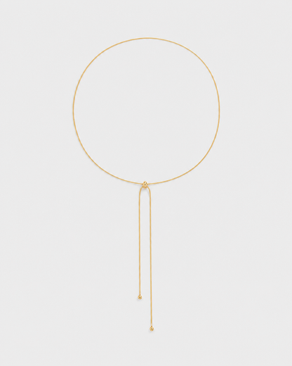 Vela fine gold slider lariat necklace on a seamless pale dove-grey studio background