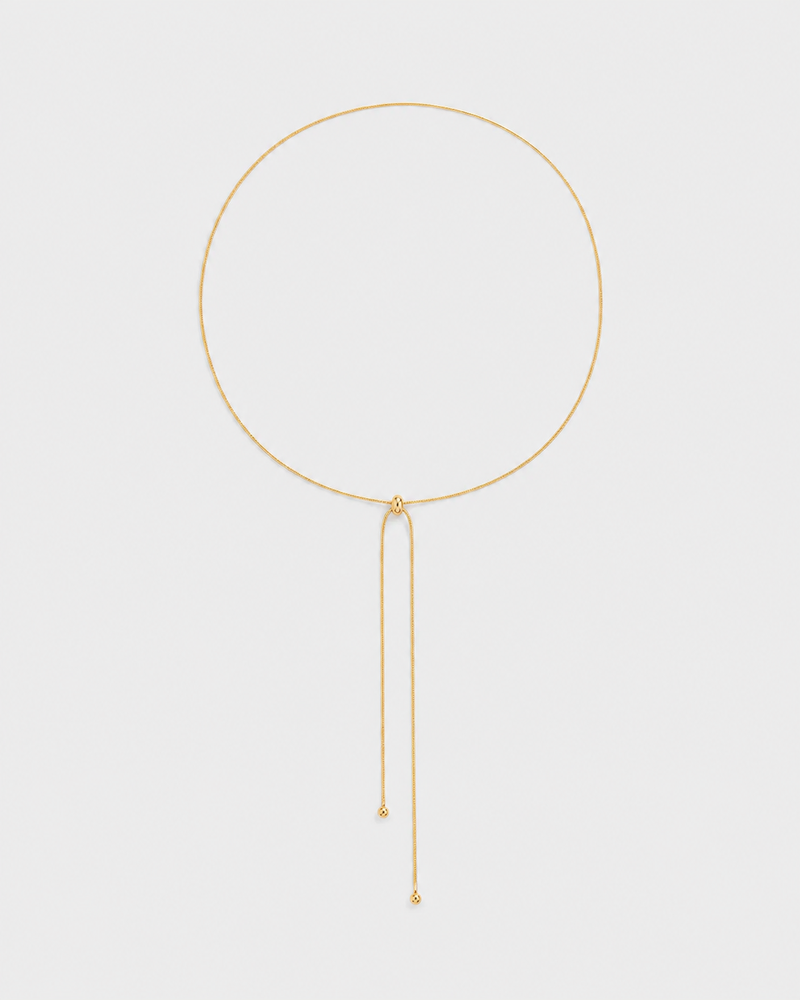 Vela fine gold slider lariat necklace on a seamless pale dove-grey studio background