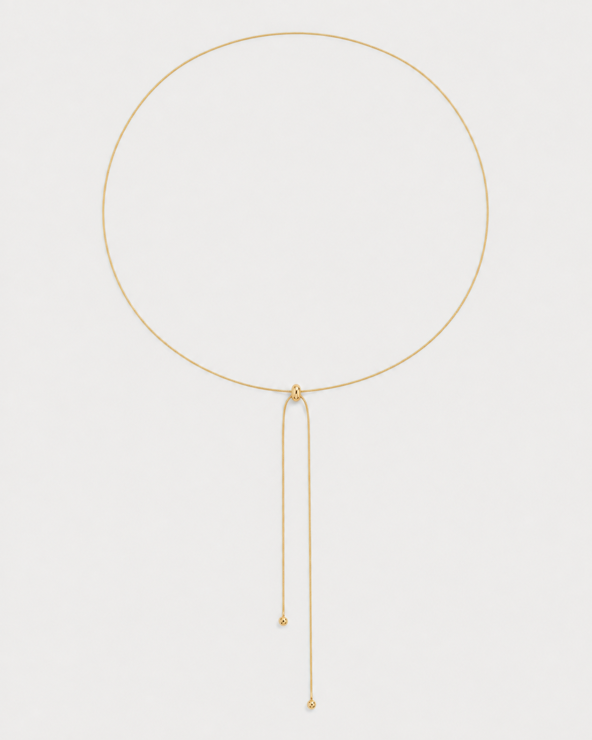 Alternate full-length view of the fine gold Vela slider lariat on pale dove-grey