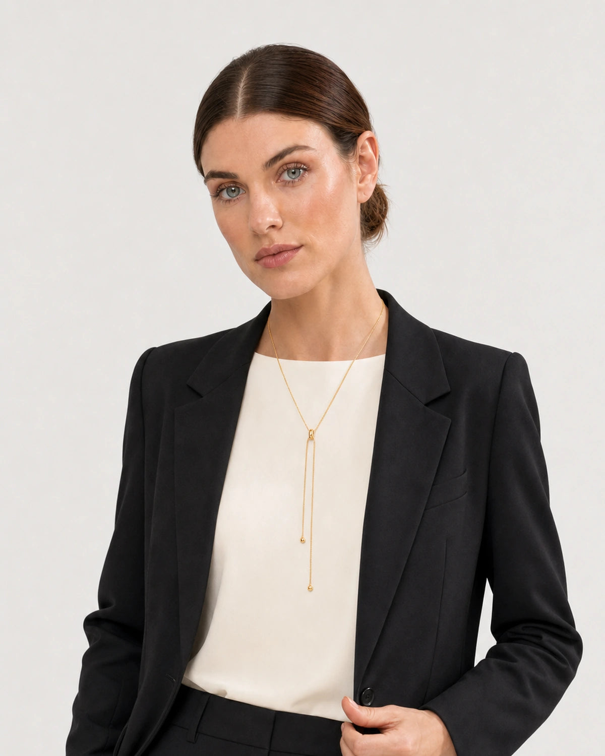Human-scale studio view of the Vela gold slider lariat worn with black tailoring