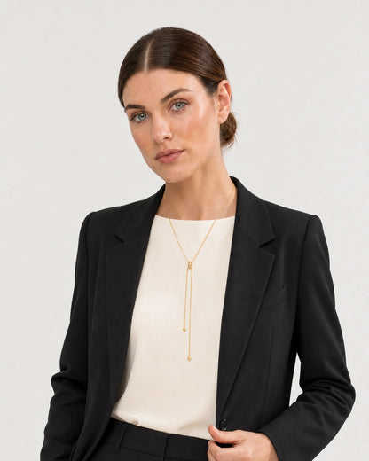 Human-scale studio view of the Vela gold slider lariat worn with black tailoring