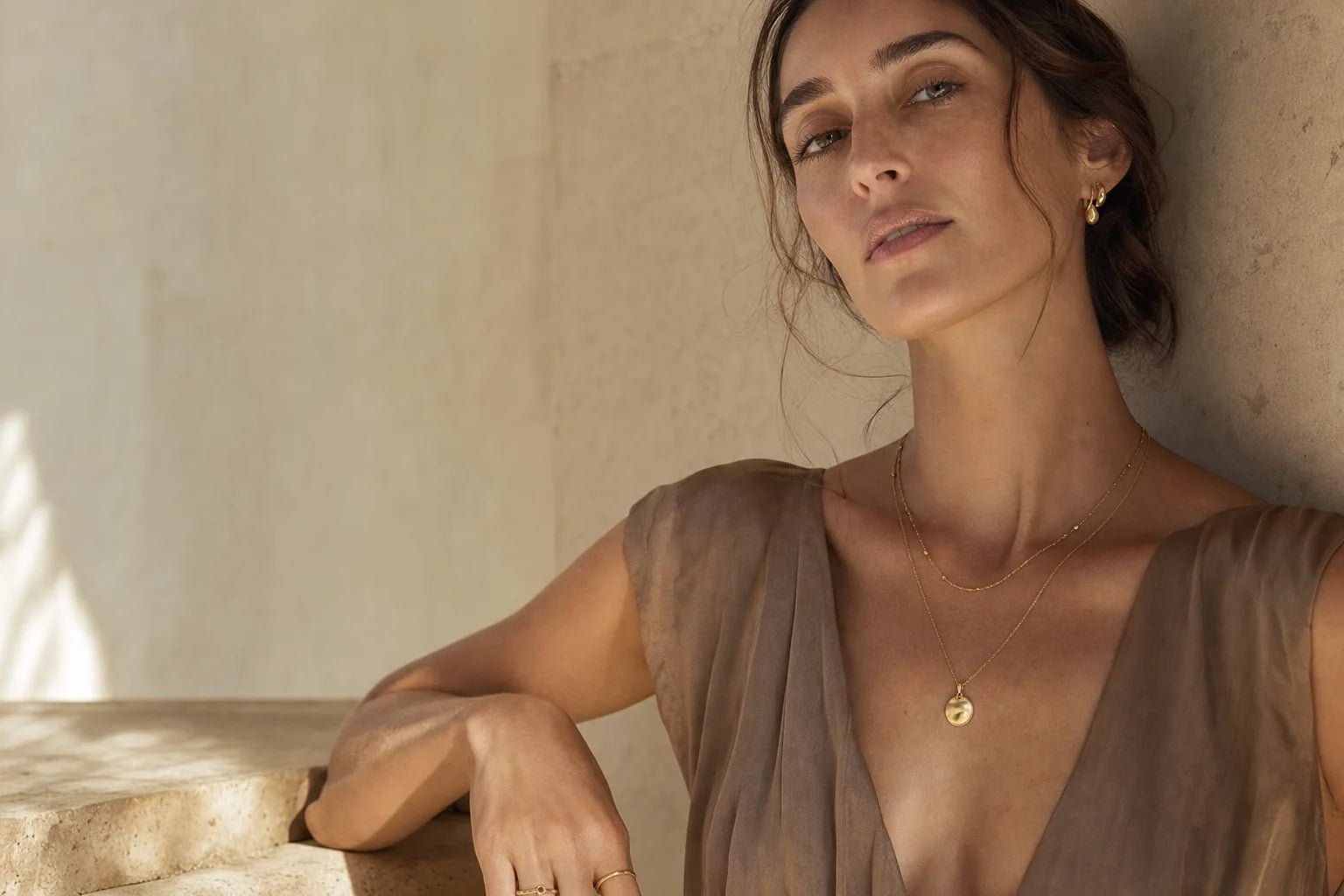 Woman wearing layered Valoraie gold jewellery in warm natural light